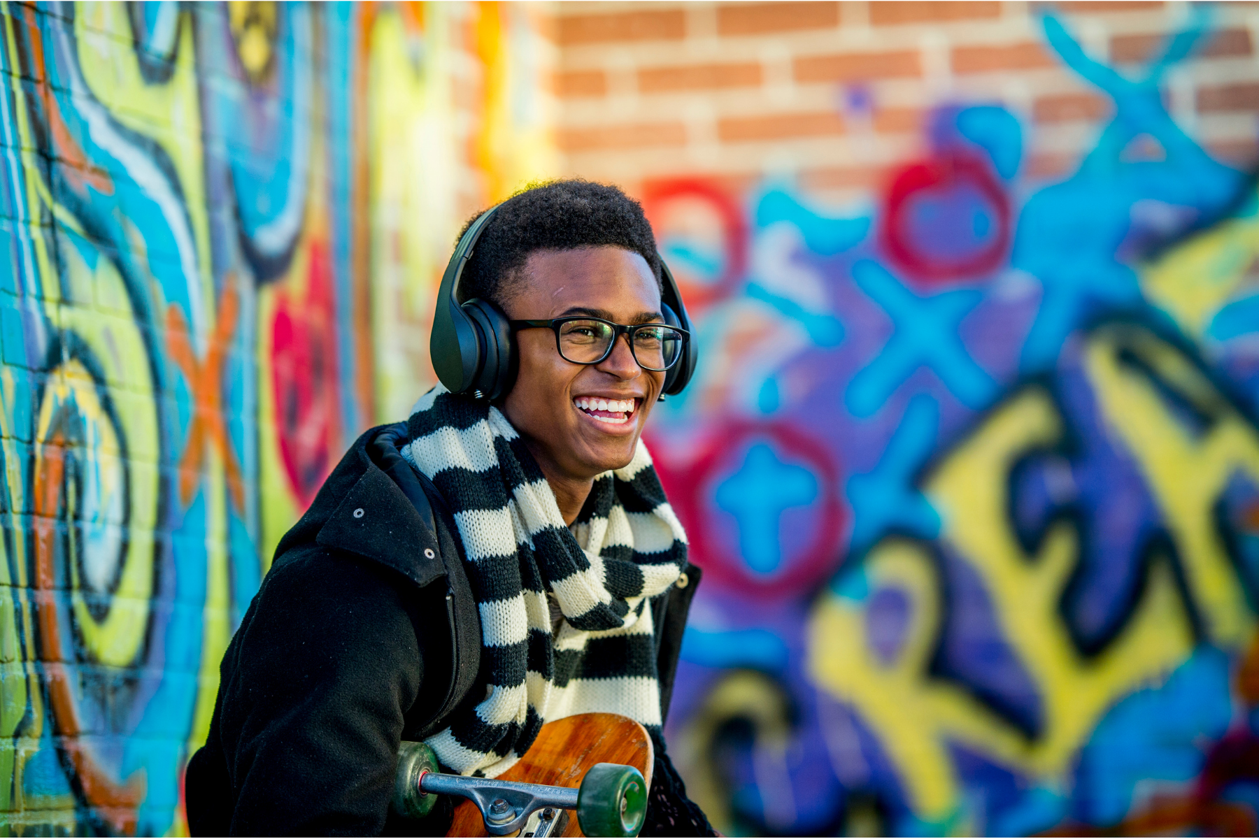 A teen boy smiling wearing headphones in front of a colorful wall